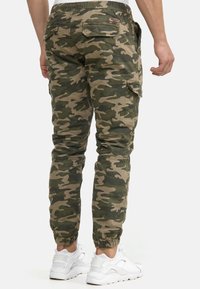 Groene camouflage cargobroek met een elastische tailleband, taps toelopende pijpen en meerdere zakken. Gecombineerd met witte sportschoenen.