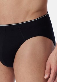 Zwarte katoenen slips met een soepele textuur, voorzien van een grijs gestreepte tailleband. Het ontwerp is naadloos aan de zijkanten voor extra comfort.