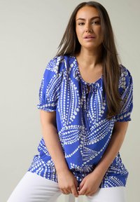 Blå bluse med hvidt prikket mønster, korte puff ærmer, rund neckline med bånddetalje, lavet af let materiale.