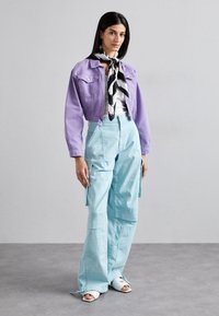 Paarse cropped spijkerjack, witte top, lichtblauwe cargobroek met zakken en een zwart-wit gestreepte sjaal. Open teen witte sandalen.