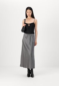 Black lace bodysuit with a front tie, paired with a long, silky gray skirt. Finished with black ankle boots and a small handbag.