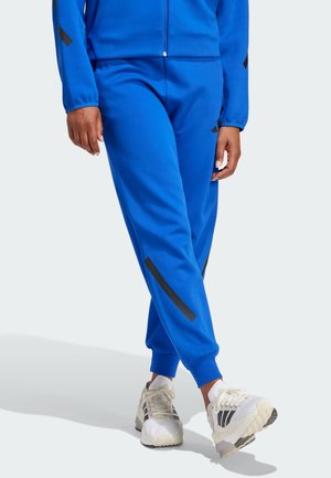 Blue jogger pants made of a smooth material with black stripes. Elastic cuffs at the ankles. Paired with white and black athletic shoes.