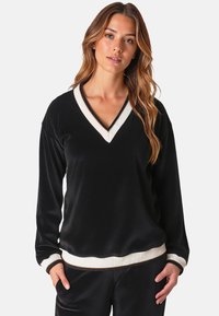 Maglietta nera a maniche lunghe con scollo a V, caratterizzata da rifiniture in crema a coste sul collo e sui polsini, con una texture liscia e un fit rilassato.