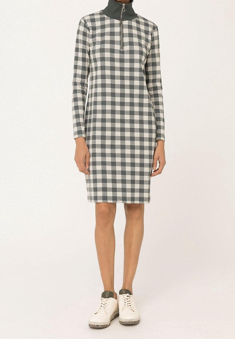 Robe à carreaux en gris et blanc, avec un col zippé montant et des manches longues. Fabriquée en tissu texturé, associée à des baskets blanches.