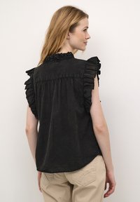 Must mustriga top mustade lühikeste varrukatega, millel on ruffle detailid õlgade lähedal, kõrge kaelus ja kokku volditud seljaosa, valmistatud pehmest, tekstuurist kangast.