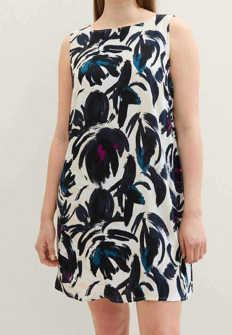 Robe sans manches à motif floral sur fond blanc. Présente des motifs floraux en bleu foncé, sarcelle et violet. Confectionnée en tissu léger.