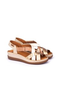 Sandalias de cuero trenzado con una combinación de colores beige y dorado, que cuentan con una suela plana, una correa en el tobillo y costuras decorativas a lo largo del borde.