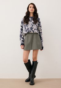 Gebreid marineblauw en wit bloementrui, grijze A-lijn rok en zwarte kniehooglaarzen, die zachte texturen en contrasterende kleuren laten zien.