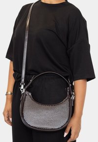 Bolso de cuero marrón con forma curva, embellecido con tachuelas plateadas. Incluye una correa larga y un acabado liso y brillante.