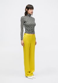Top de manga larga con estampado en blanco y negro y cuello alto, combinado con pantalones amarillos de tiro alto y pierna recta, y zapatos blancos puntiagudos.