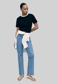 Black t-shirt with a contrasting neckline, light blue straight-leg jeans, white wrap tied at the waist, and white flip-flops.