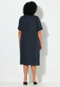 Tmavěmodré šaty s krátkým rukávem a texturovanou tkaninou, ke kolenům, s plisovaným zadním dílem a uvolněným střihem, doplněné černými lodičkami na podpatku.