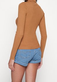 Haut marron côtelé à manches longues avec un col montant, associé à un short en denim bleu clair avec un ourlet replié et un détail de couture sur la poche arrière.