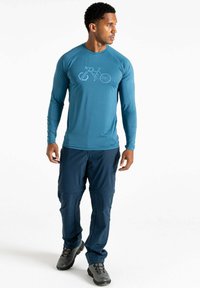 Langärmliges, türkisfarbenes Sportshirt mit einem Fahrrad-Graphic auf der Vorderseite, kombiniert mit navyfarbigen Cargo-Hosen und robusten schwarzen Schuhen.