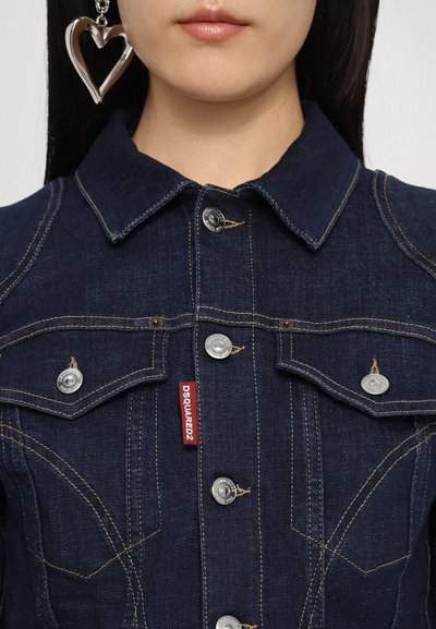 Dark denim jacket with classic collar, silver buttons, and red brand tag. Features chest pockets and visible stitching details.