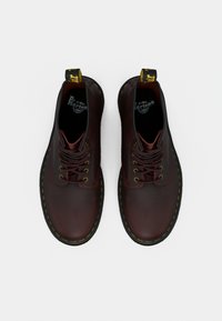 Μπορντό δερμάτινα παπούτσια με κορδόνια, με λεία υφή, κίτρινη ραφή, στρογγυλή μύτη και μαύρη λαστιχένια σόλα. Διαθέτουν θηλιά στην φτέρνα.