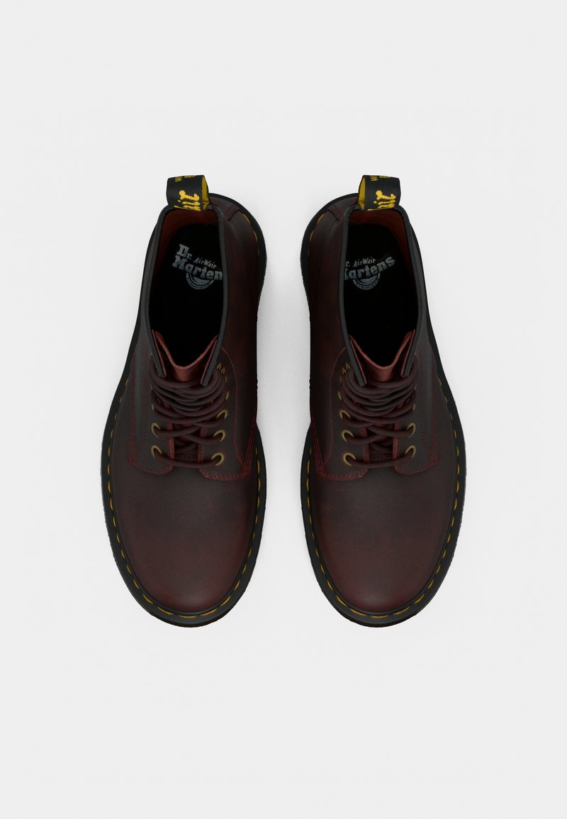 Chaussures à lacets en cuir marron avec une texture lisse, une couture jaune, un bout rond et une semelle en caoutchouc noire. Elles sont dotées d'une languette à l'arrière.