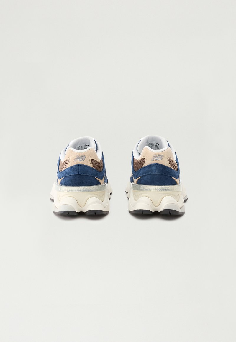 Niebieskie zamszowe sneakersy z beżowymi akcentami, z miękką podeszwą i teksturowanym tyłem. Posiadają białą kołnierz i odblaskowy srebrny detal.