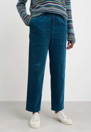 Pantalons en velours côtelé bleu avec une coupe décontractée, deux poches avant et une taille avec cordon de serrage, associés à des baskets beige.