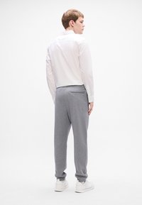 Pantalones de chándal grises ajustados con bolsillos laterales, puños elásticos y un bolsillo trasero, combinados con una camisa blanca ajustada de botones.