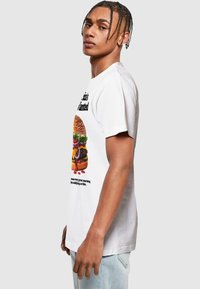 Hvid bomulds T-shirt med et grafisk motiv af en farverig hamburger med salat, ost og tekst under. Korte ærmer, afslappet pasform.