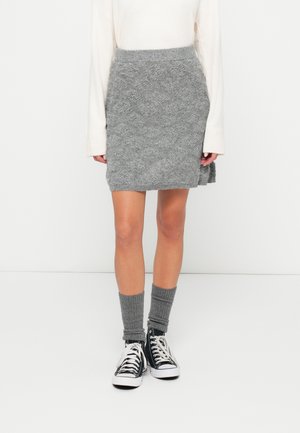Jupe en tricot gris avec un motif texturé, taille haute et fente sur le côté, associée à des chaussettes côtelées grises et des baskets en toile noires.