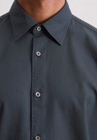 Donkergrijze button-up shirt gemaakt van gladde stof, met een puntkraag en zilverkleurige knopen met een stervormig ontwerp.