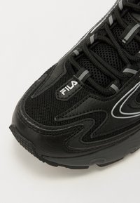 Black sneaker featuring a mix of mesh and leather materials, prominent curved design lines, grey accents, and lacing system with Fila logo.