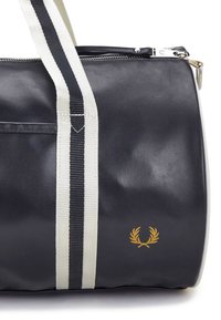 Zwarte sporttas met witte gestreepte hengsels, ritssluiting en gouden logo-embleem. Gemaakt van duurzaam materiaal met een gladde textuur.