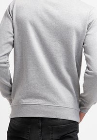 Šedá mikina s dlouhými rukávy, kulatým výstřihem a žebrovanými manžetami. Měkká textura a jednobarevná bez viditelných log nebo vzorů.