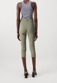 Zelené krátké kalhoty mají střih na míru, vysoký pas a hladkou texturu. Kombinovány jsou s šedým tílkem a černými sandály na širokém podpatku.