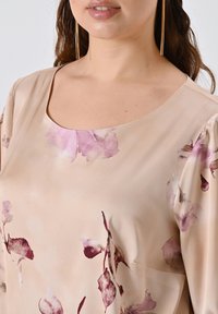 Blusa beige chiaro con scollatura quadrata, caratterizzata da motivi floreali in tonalità rosa e bordeaux, e tessuto morbido e testurizzato.