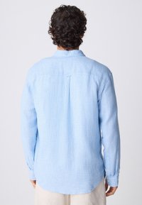 Helevalge pikkade varrukatega särk, millel on tekstuuriga kude, nööbitavad mansetid ja tagumine voldik. Kaarekujuline hem lisab lõdvestunud väljanägemise disainile.