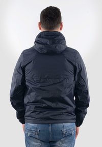 Giacca leggera blu navy con cappuccio, caratterizzata da una texture liscia e lucida e polsini elasticizzati, indossata con jeans blu.