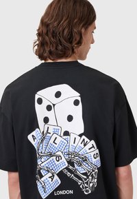 Black T-shirt featuring a graphic of visible dice and playing cards held by a skeletal hand, with blue and white checkerboard details.