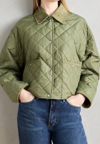 Quilted grøn jakke med en kordfløjlskrave, trykknapper og forlommer. Har en boxy fit med struktureret stof og en kort længde.