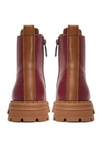 Botas de tobillo de cuero rojo con paneles laterales marrones y cremalleras, que cuentan con una suela de goma texturizada gruesa de color marrón claro. Detalles de costura en todo el calzado.