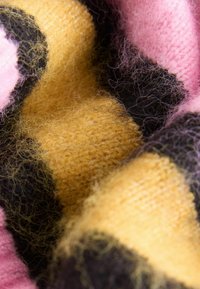 Soft knitted fabric texture with yellow, black, and pink color blocks, showing fine fibers and a fuzzy surface.
