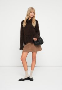 Cárdigan de punto marrón con cierre de botones, atado a la cintura. Combinado con una mini falda de ante marrón y un bolso negro. Bailarinas negras y calcetines beige.