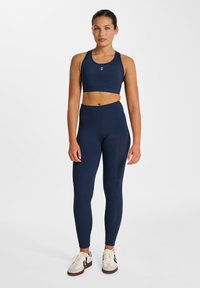 Marinblå sportstopp och högmidjade leggings i ett mjukt, stretchigt tyg, kombinerade med neutrala träningsskor, med en enkel logotyp.