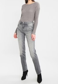 Top de manga larga de canalé gris combinado con vaqueros rectos en gris claro. El conjunto se complementa con botines negros de punta. 