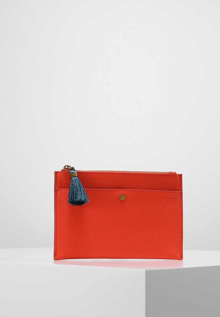 Sac clutch rectangulaire rouge avec poche avant, petit bouton rond doré, fermeture éclair supérieure et tirette avec pompon bleu sarcelle, exposé sur un socle blanc.