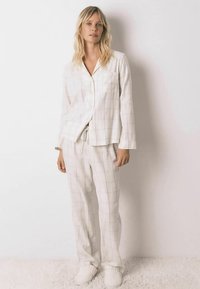 Ensemble de pyjama à carreaux blancs avec manches longues et chemise à boutons. Comprend une poche poitrine et un pantalon à cordon de serrage. Texture douce. Chaussons inclus.