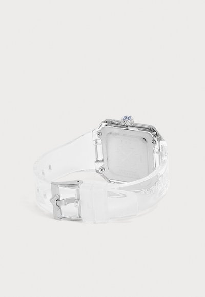 Montre transparente avec un dos carré argenté, une couronne accentuée de bleu et un bracelet transparent à boucle, présentée sur fond blanc.