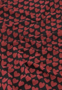 Schwarzer Stoff mit einer strukturierten Oberfläche, der ein sich wiederholendes Muster aus roten Herzen zeigt, die in unterschiedlicher Größe gleichmäßig über das Material verteilt sind.