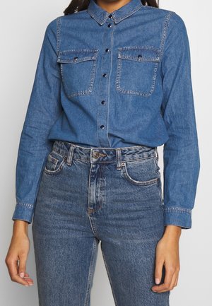 Spijkerblouse met kraag, twee borstzakken en knoopsluiting aan de voorkant. Lange mouwen, in een medium blauwe wassing, met subtiele stiksel-details.