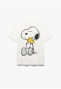 T-shirt en coton blanc avec une illustration en contour noir de Snoopy souriant en train d'enlacer Woodstock au dos. Manches courtes, coupe décontractée.