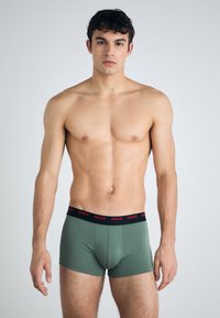 Grüne Baumwoll-Boxershorts mit einem schwarzen Bund, der mit dem roten "HUGO"-Logo versehen ist. Die Passform ist eng anliegend, mit einer glatten Textur und einem schlichten Design.