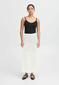 Haut sans manches noir associé à une longue jupe blanche en dentelle à motif floral. La jupe a une coupe fluide et une taille cintrée.