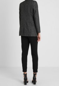 Grå ullblazer med skräddarsydda axlar, i kombination med svarta tapered byxor och svarta ankelstövlar med klack, vy från baksidan.